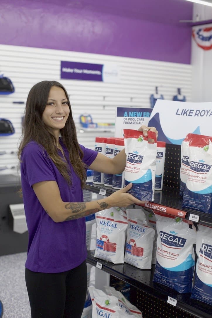 A Purple Frog Pool Supply team member in a purple polo stocking professional-grade Regal pool chemicals on the store shelves