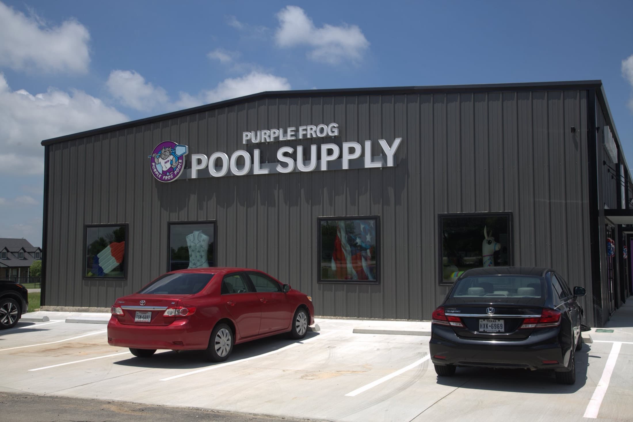 The Purple Frog Pool Supply storefront in Aledo, TX — a gray metal building with the Purple Frog logo sign and cars parked out front under a blue sky