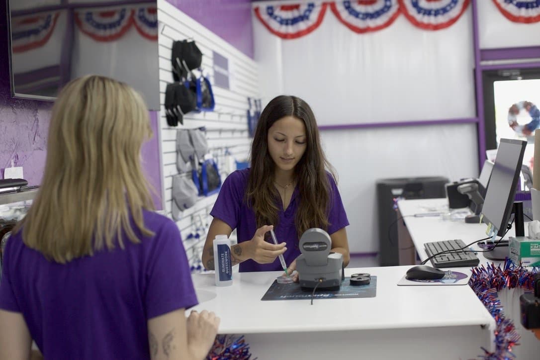 A Purple Frog Pool Supply team member running a water test on an electronic meter at the front counter while helping a customer